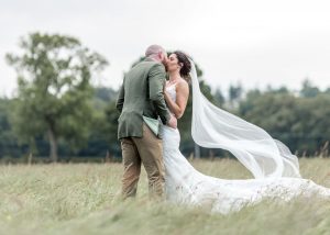 Bride and groom kissing in a field. Dress blowing in the wind.